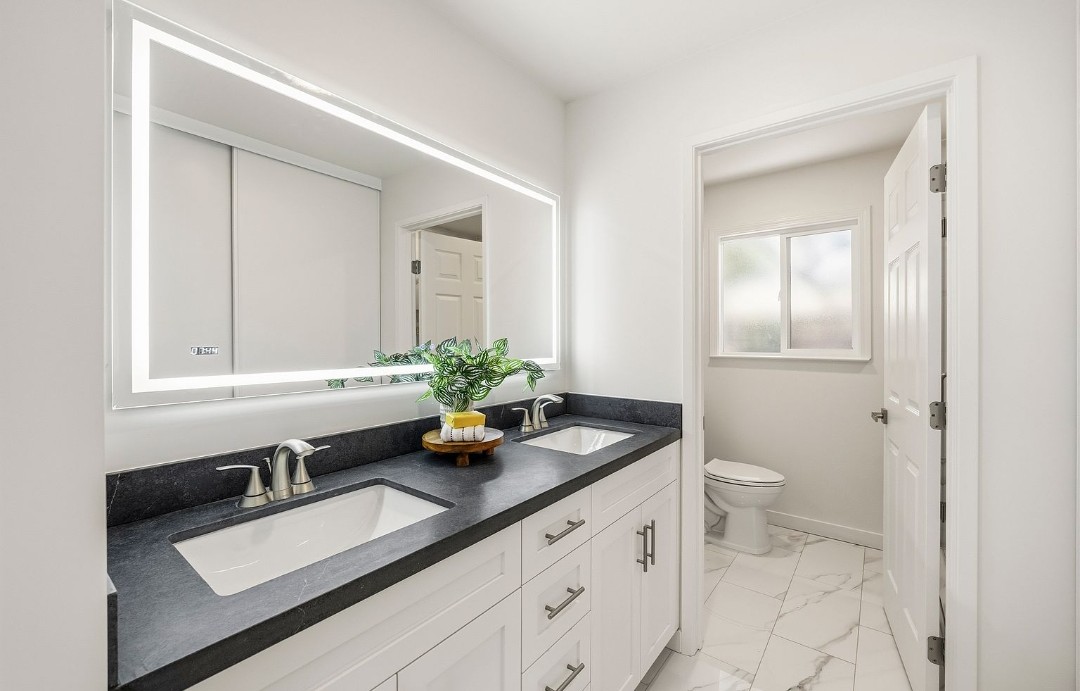 Remodeled bathroom with double vanity and backlit mirror